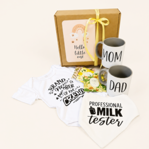 Hello Little One new baby gift hamper featuring a short-sleeved baby grow, Mom and Dad mugs, three tea sachets, a bib and a kraft gift box.