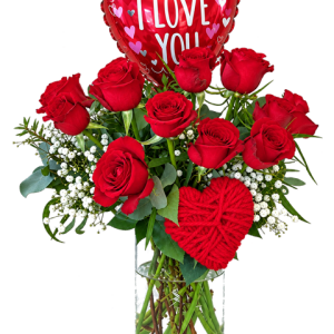 A dozen red roses in a glass vase with an I Love You balloon and decorative red heart