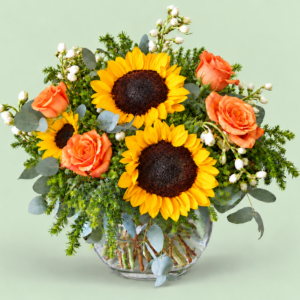Yellow sunflowers and orange roses arranged with greenery in a vase. Vase style may differ.